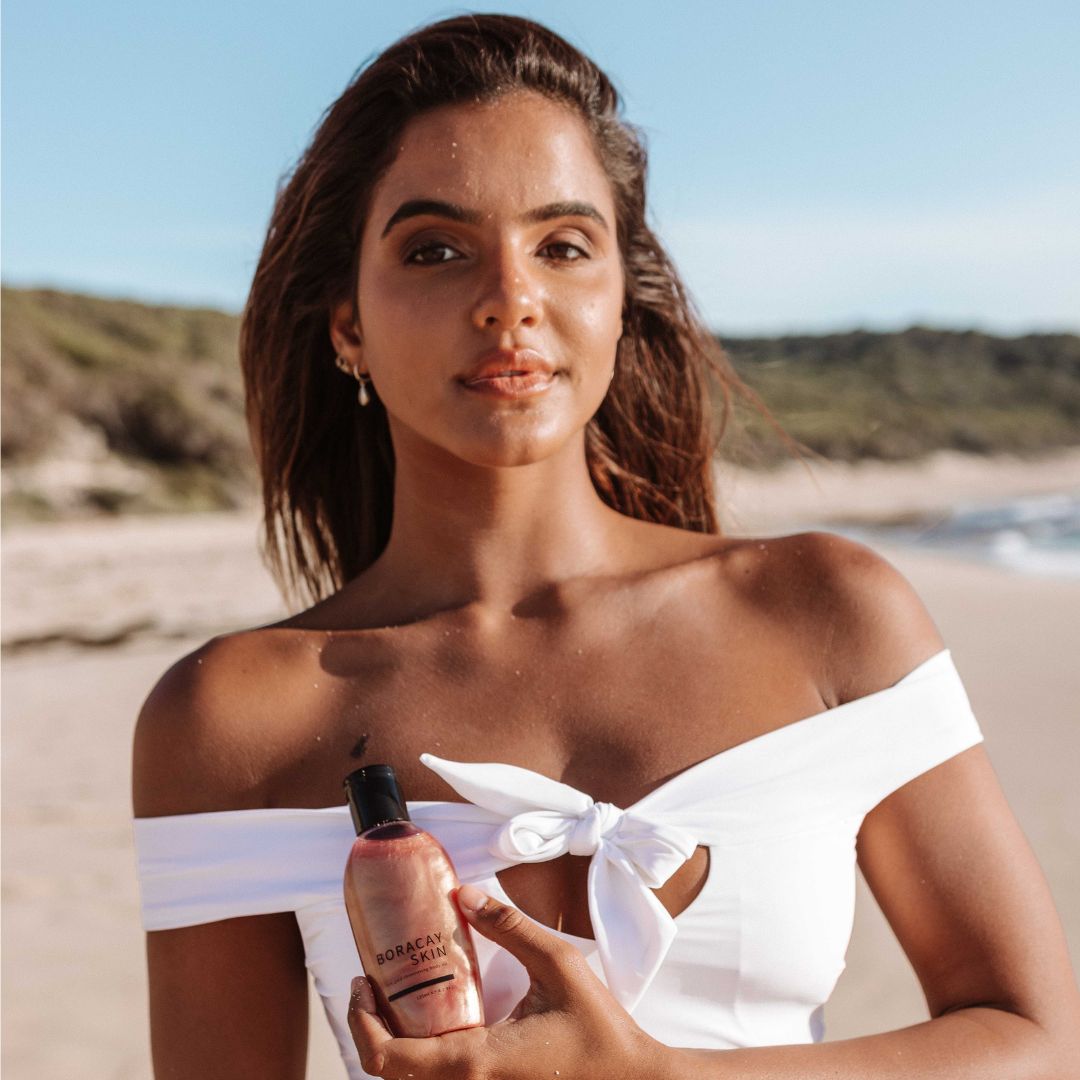 Model smiling and holding Boracay Skin Rose Gold Shimmering Body Oil at the beach