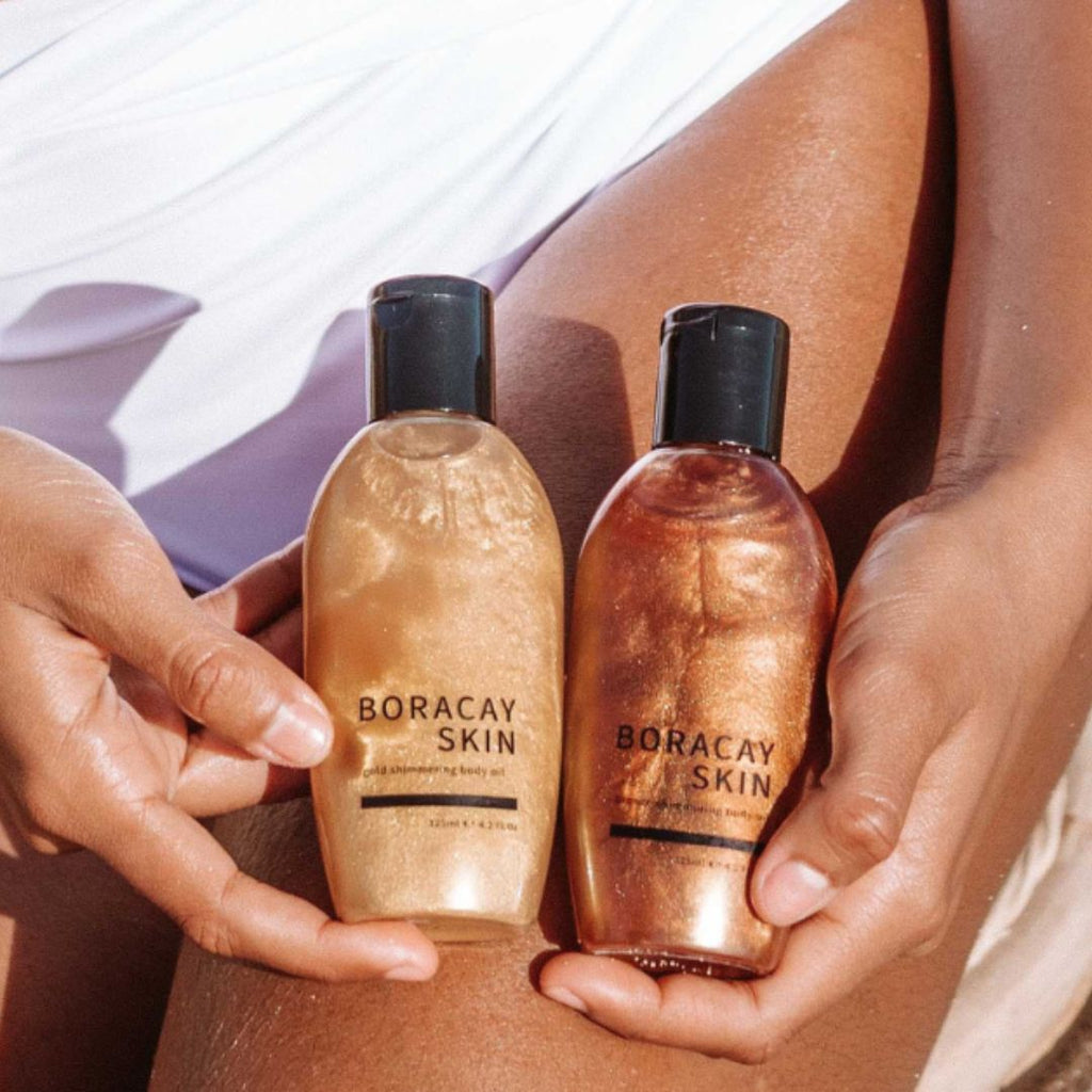 Boracay Skin Shimmer Bundle Bronze and Gold body oils held by model next to her leg while at the beach